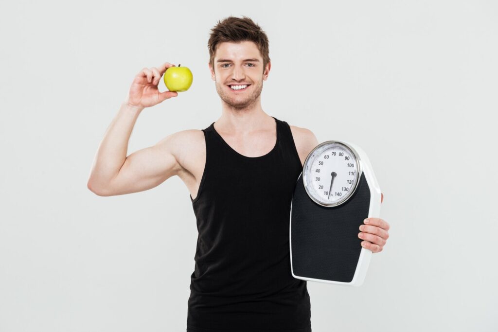 smiling-young-sportsman-holding-scales-apple